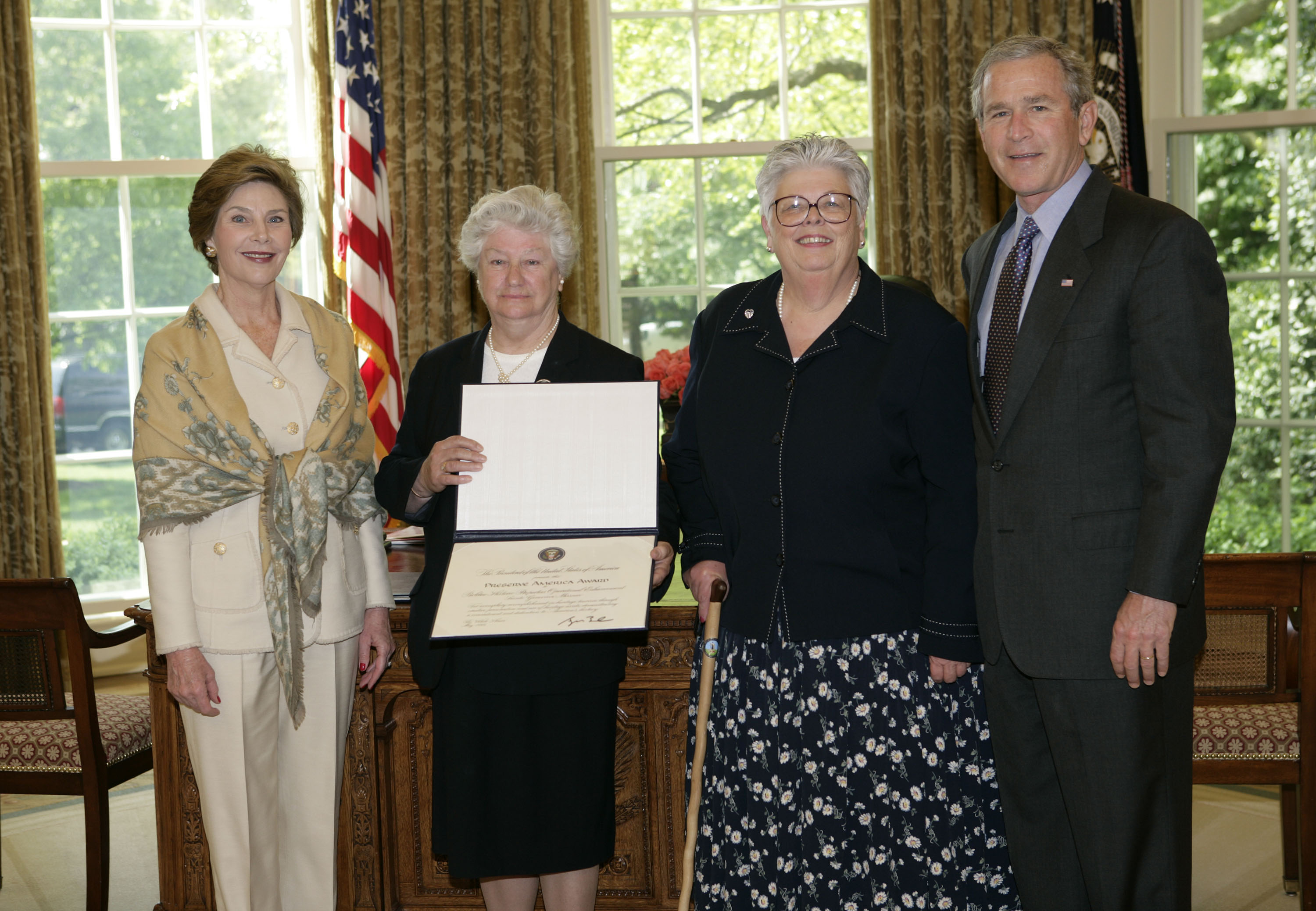 President George W. Bush and Laura Bush present the 2005 Preserve America Presidential Award to Agnes Chouteau, President, The National Society of the Colonial Dames of America, left, of St. Louis and Lorraine Stange, Director, Bolduc Historic Properties, of Sainte Genevieve, Missouri, in the Oval Office Monday, May 2, 2005.( White House photo by Eric Draper)