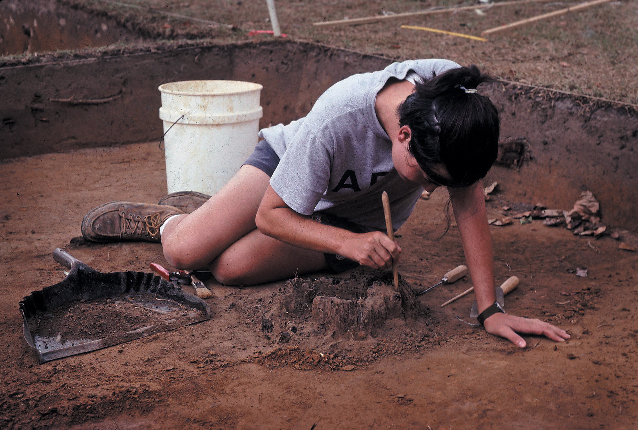 Graduate student carefully excavates the remains of a charred post.