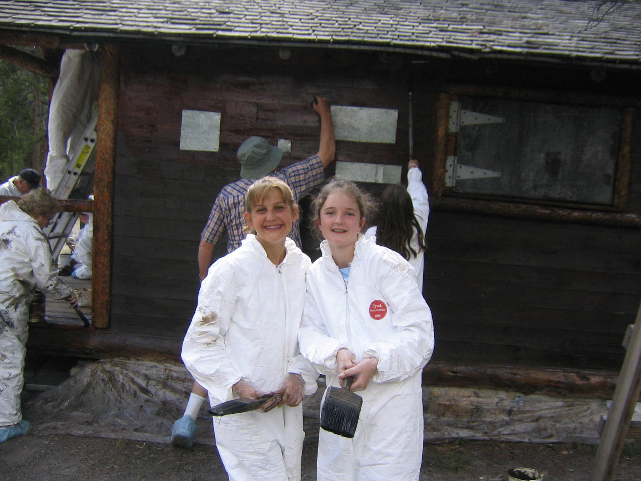 Two young guest volunteers at Yellowstone participate in staining a historic cabin.