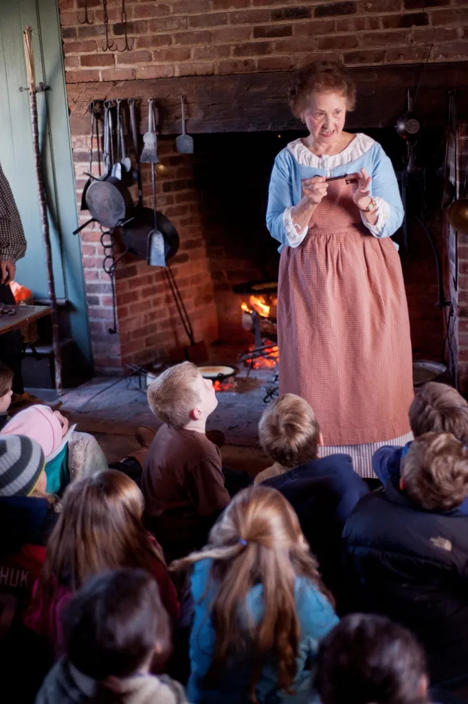 A costumed docent interprets 18th-century life for a school tour.