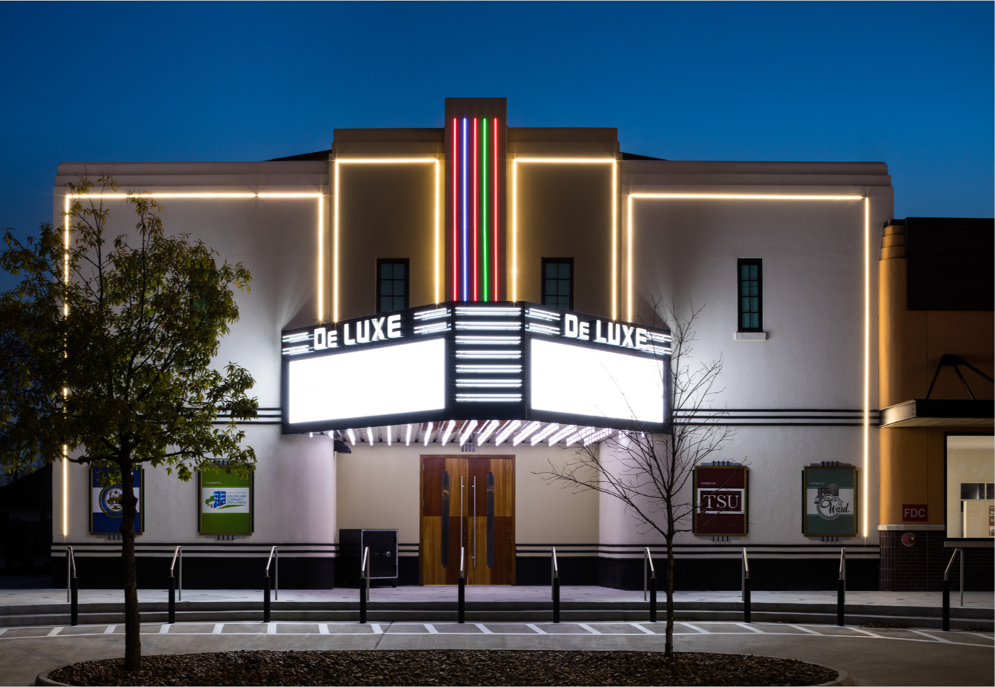 Exterior of DeLuxe Theater. Depicts the theater lights on. The marquee is blank and the name De LUXE is illuminated above it.